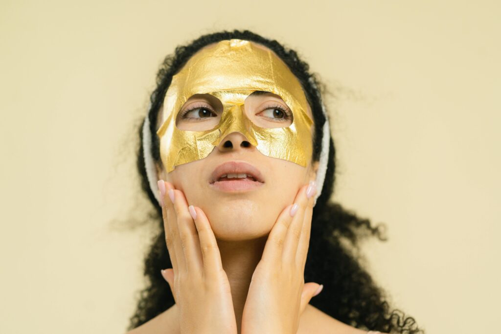 Close-up of woman wearing a gold sheet mask for skincare in a studio setting.